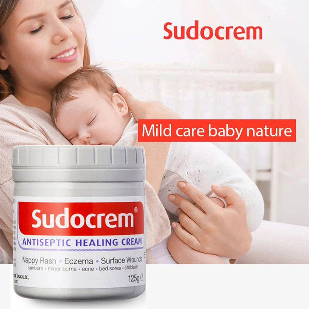 Woman holding a baby with a jar of Sudocrem Antiseptic Healing Cream in the foreground.